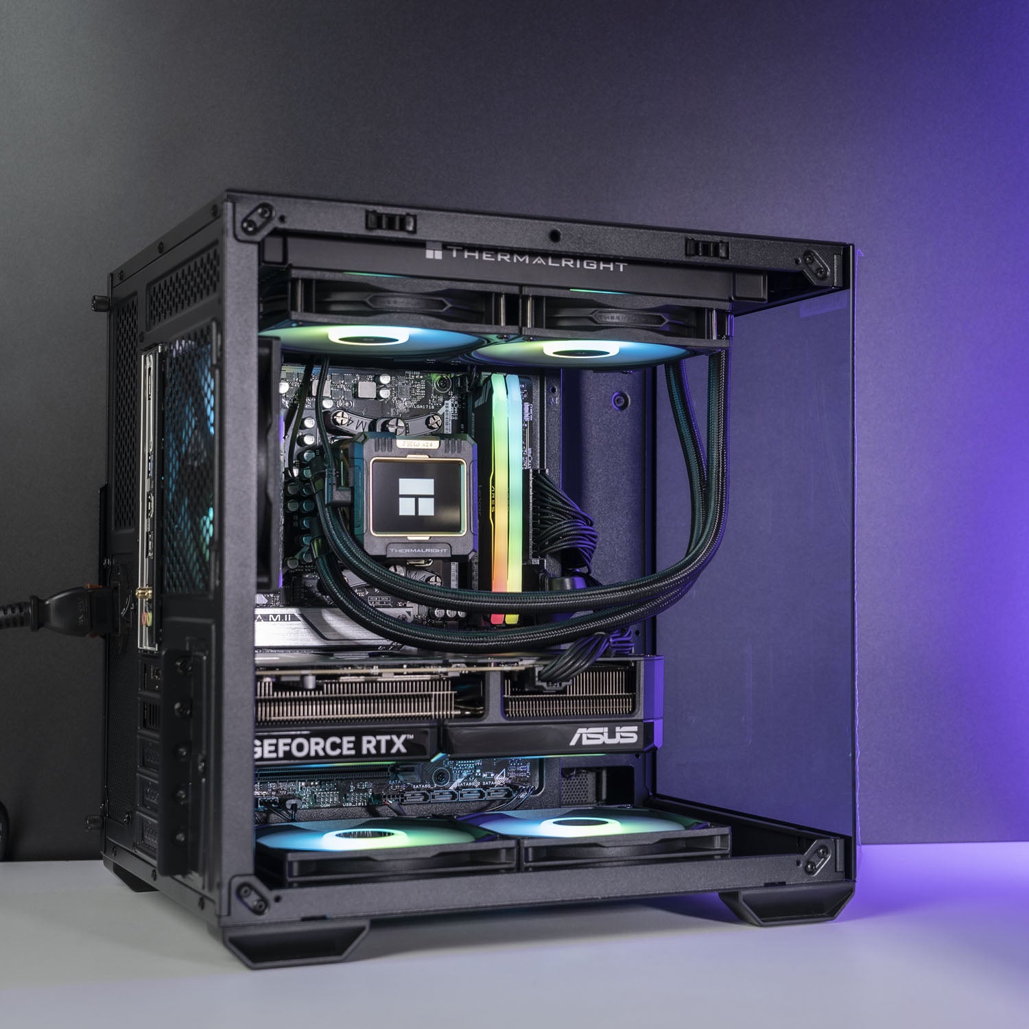 A high-end custom PC build in a black Thermaltake case with a clear side panel, showcasing internal components including an ASUS GeForce RTX graphics card, a liquid cooler with RGB lighting, and dual CPU coolers, set against a dark gray studio background.