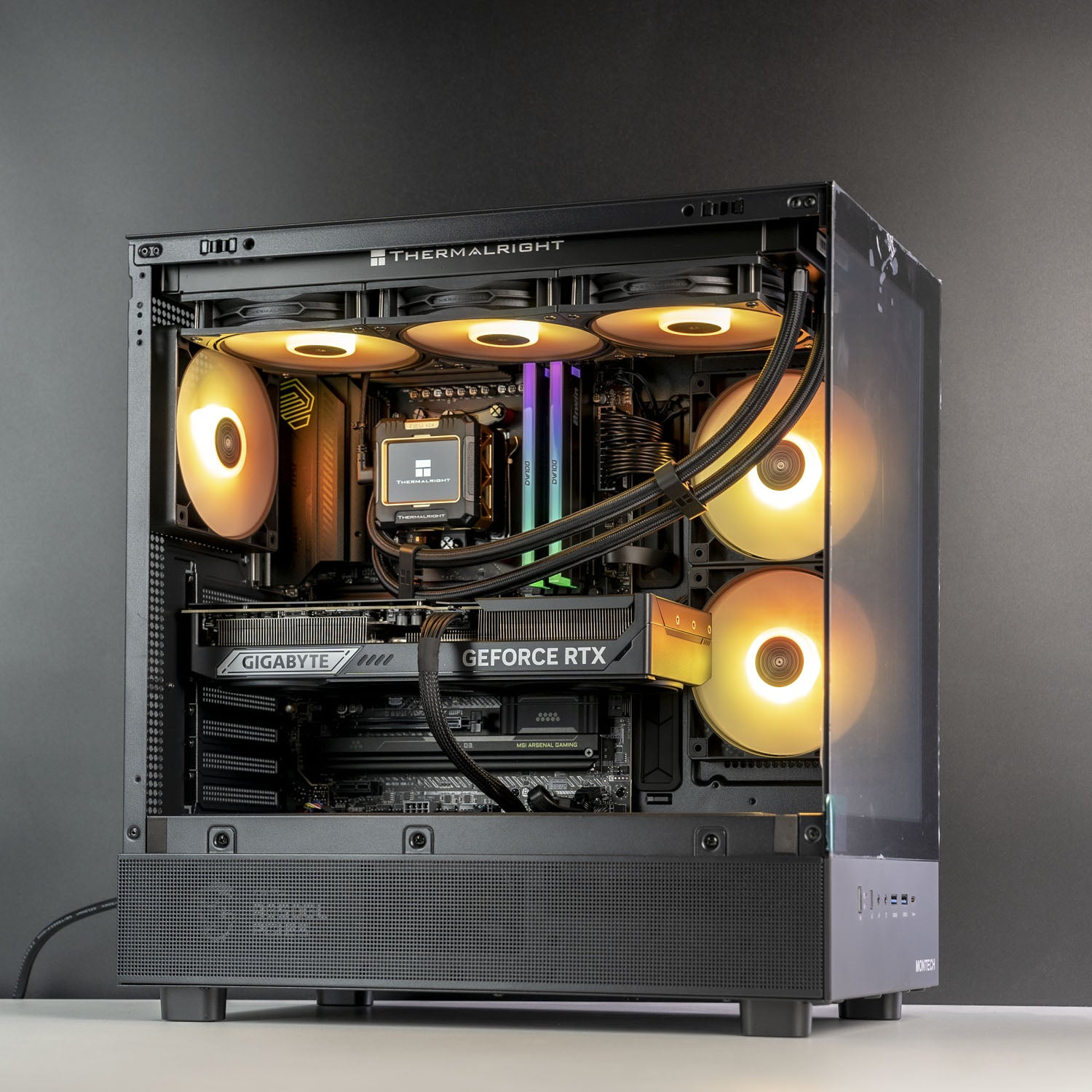 A custom-built desktop PC inside a Thermalright case, featuring a black side-panel design, liquid cooling with glowing amber fans, and a Gigabyte RTX graphics card, set against a dark gray studio background.