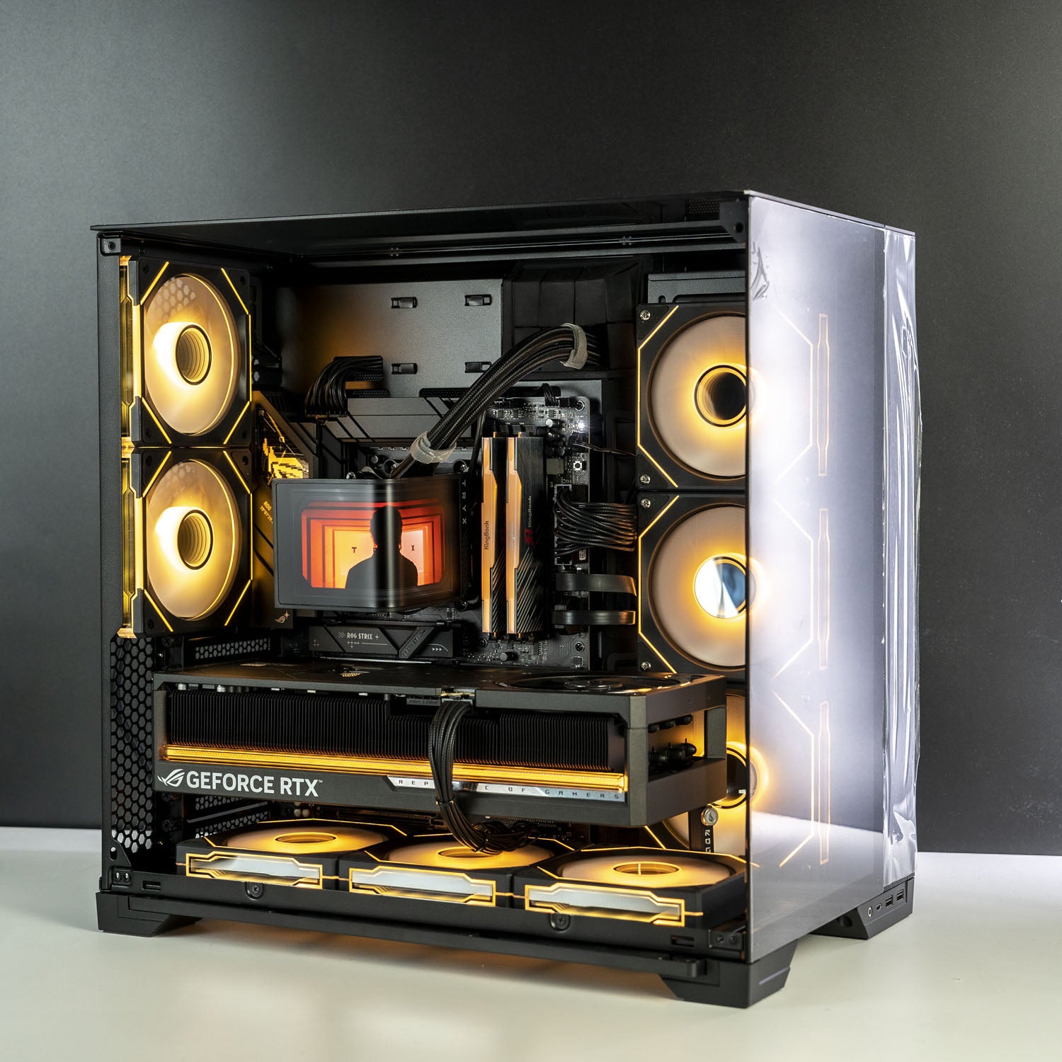 A custom-built desktop computer inside a black mid-tower case with a clear side panel, showcasing an intricate internal setup with glowing yellow and orange RGB fans, a liquid CPU cooler, and a GeForce RTX graphics card, set against a dark gray background.
