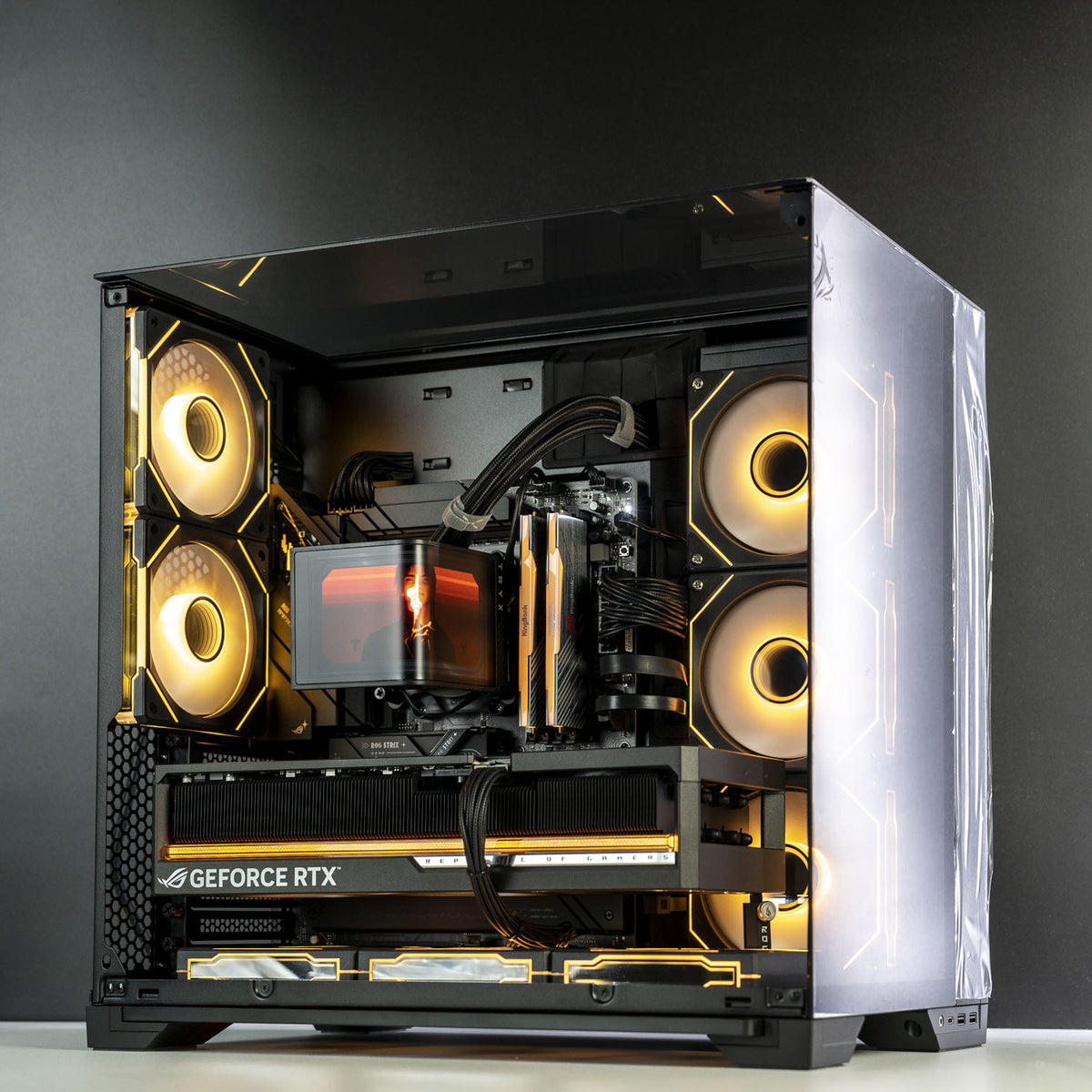 A high-end gaming PC with an open side-panel case, showcasing a custom liquid CPU cooler, dual RTX graphics cards, and three large RGB fans glowing with warm yellow light against a dark gray background.