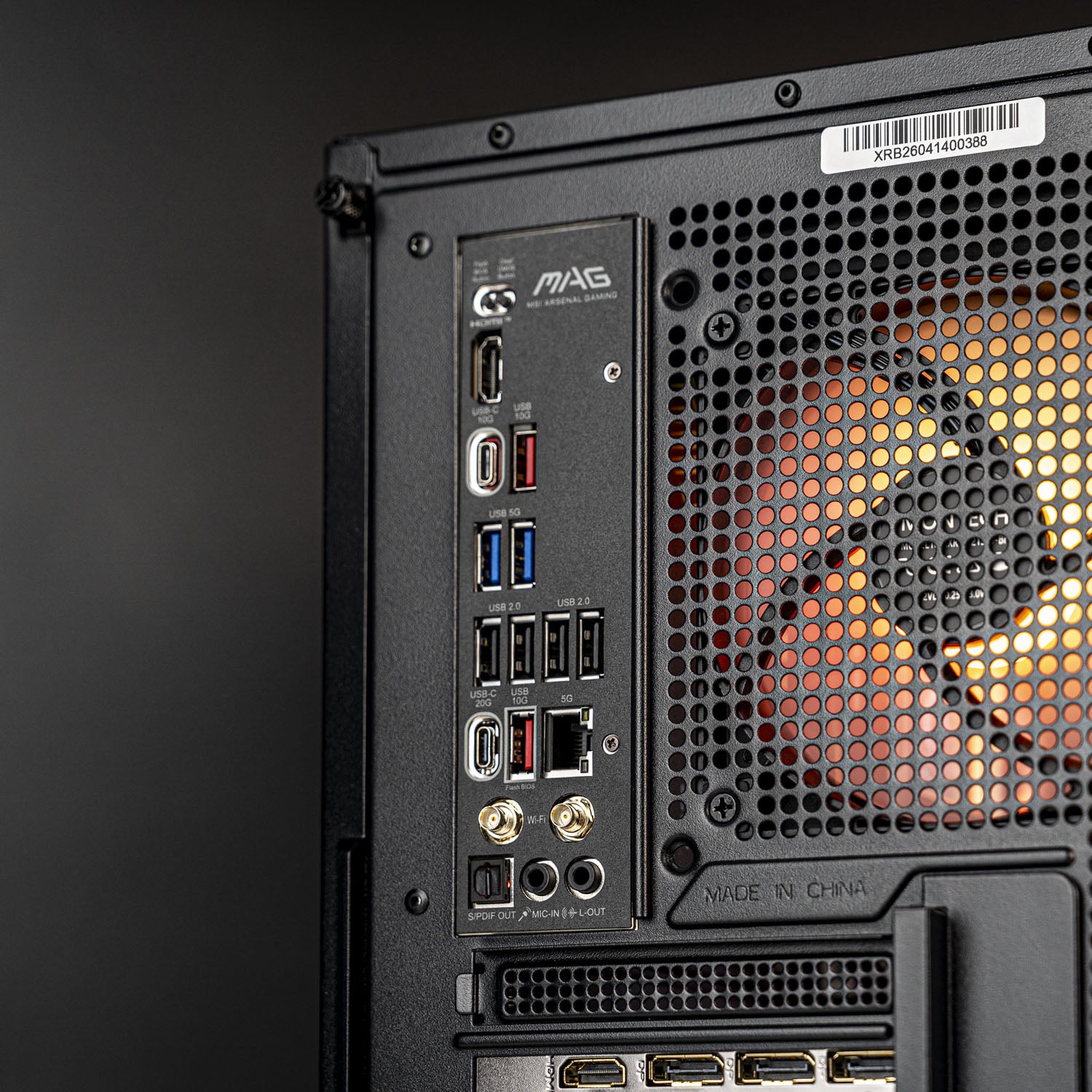 Close-up of the rear I/O panel of a black MAG desktop PC case, showing various ports including USB, HDMI, DisplayPort, and Ethernet, next to a perforated metal fan grille.